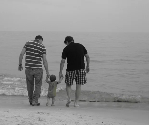 Two adults and a child standing together at the water's edge on a beach