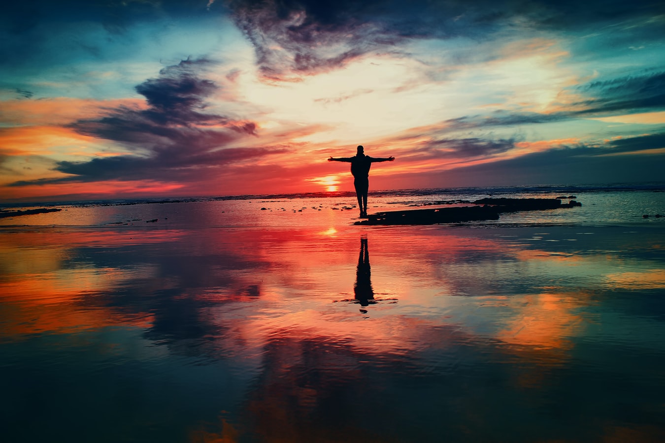 Person feeling the power of a strong sense of self with arms outstretched standing on the beach at sunset