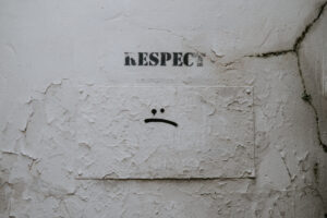 Cracked wall painted with with the word respect sloppily stenciled on it.