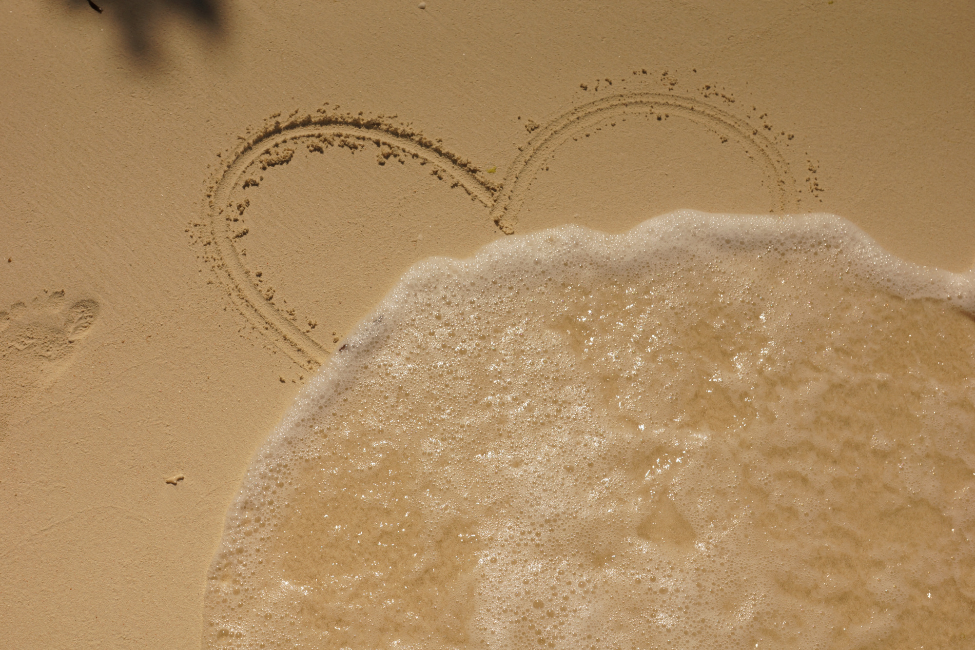 Wave washing over a heart carved in the sand.