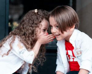 Little girl whispering to a little boy.