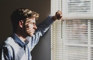 Man looking out a window as he contemplates how he'll tell his wife he's been cheating.
