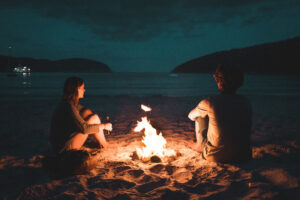 Couple sitting by a campfire on the beach discussing how to fight fair in marriage.