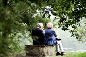 Older couple sitting on the bank of a river enjoying a glass of wine.