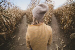 Woman standing at a crossroad in a corn field considering which direction to turn.