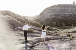 Couple struggling to continue to hold hands as they walk on either side of a small stream.