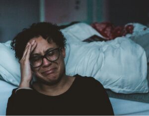 Woman crying against her bed while her partner sleeps because of the emotional neglect she feels in her marriage.