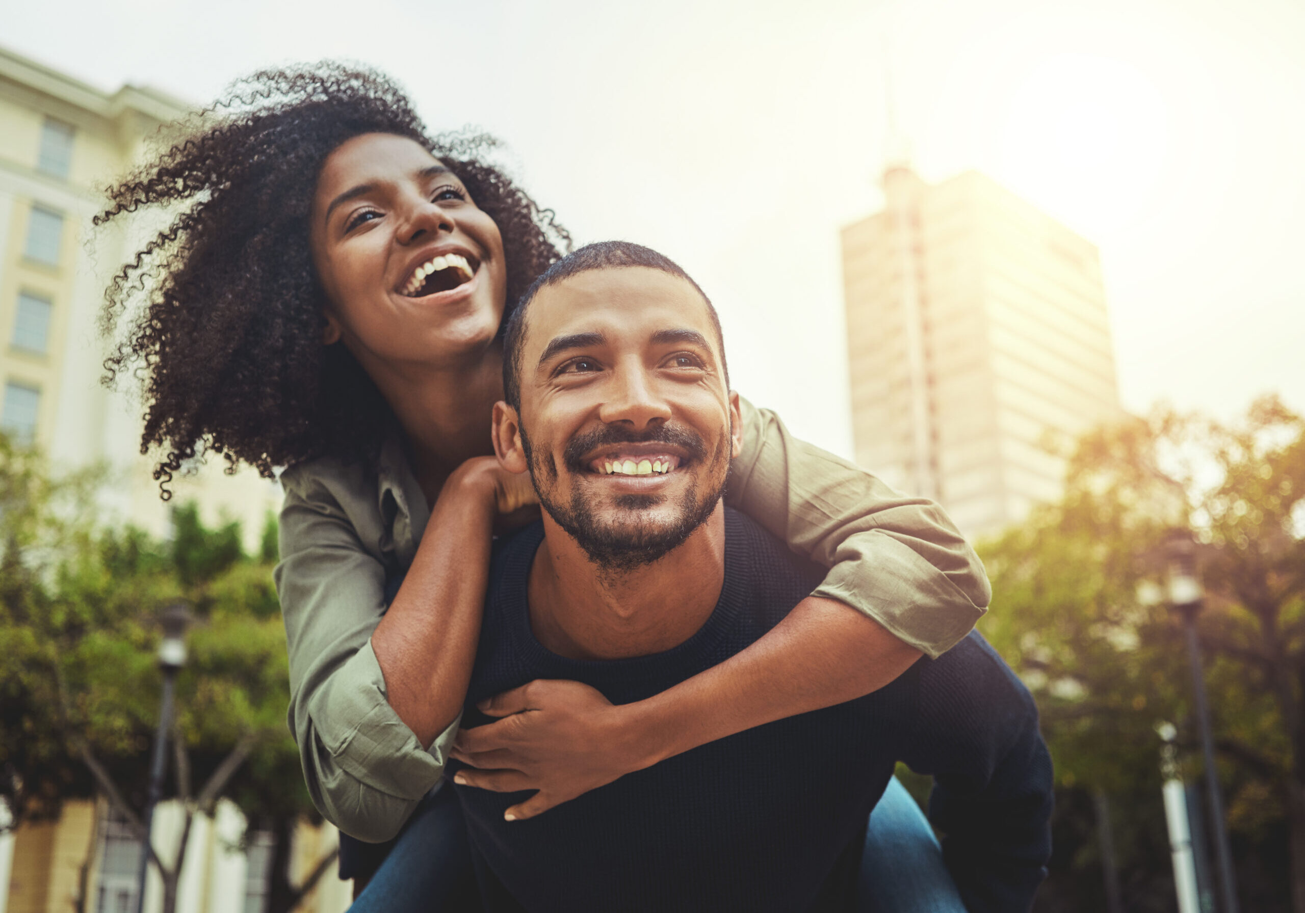 Young couple in love having fun in the city Cheerful young man giving piggyback ride to his girlfriend outdoors in the city
